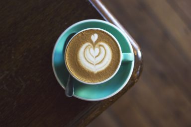 Tasse mit Cappuccino und Herz-Latte-Art auf einem grünen Unterteller.